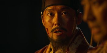 Movie still from “Kingdom” (2019), created by Eun-hee Kim – A person with a beard and a hat on; Close Up shot, Over the shoulder angle