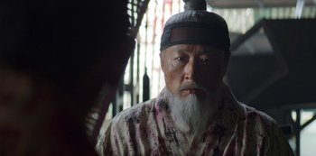 Movie still from “Kingdom” (2019), created by Eun-hee Kim – An older man with a beard and a hat; Close Up shot, Over the shoulder angle