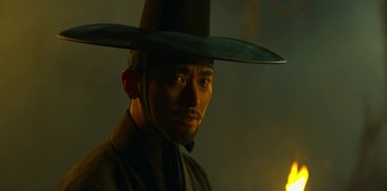 Movie still from “Kingdom” (2019), created by Eun-hee Kim – A man wearing a black hat and a black coat; Close Up shot, Low angle