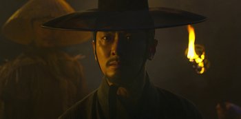 Movie still from “Kingdom” (2019), created by Eun-hee Kim – A man wearing a black hat and a black shirt; Close Up shot, Low angle