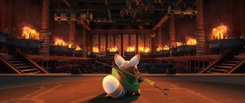 Movie still from “Kung Fu Panda 3” (2016), directed by Jennifer Yuh Nelson – A small dog is dressed in a green outfit and holding a sword in front of a fire place; Wide shot, Low angle