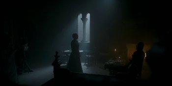 Movie still from “House of the Dragon” (2022), created by George R.R. Martin – A woman standing in a dimly - lit room next to a table; Wide shot, Low angle