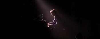 Movie still from “La La Land” (2016), directed by Damien Chazelle – A man in a purple suit is playing the piano; Wide shot, High angle