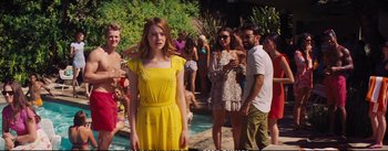 Movie still from “La La Land” (2016), directed by Damien Chazelle – A woman in a yellow dress standing in front of a group of people; Medium shot, Over the shoulder angle