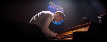 Movie still from “La La Land” (2016), directed by Damien Chazelle – A man is playing the piano in front of a stained - glass window; Medium shot, Low angle