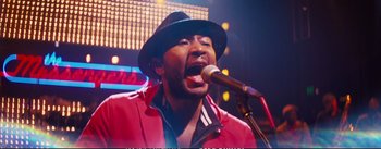 Movie still from “La La Land” (2016), directed by Damien Chazelle – A man with a hat is singing into a microphone; Close Up shot, Low angle