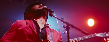 Movie still from “La La Land” (2016), directed by Damien Chazelle – A man in a red jacket singing into a microphone on a stage; Close Up shot, Low angle