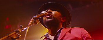Movie still from “La La Land” (2016), directed by Damien Chazelle – A man with a hat is singing into a microphone; Close Up shot, Low angle