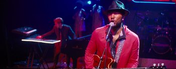 Movie still from “La La Land” (2016), directed by Damien Chazelle – A man in a red shirt is singing into a microphone; Medium shot, Over the shoulder angle