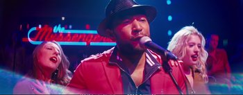 Movie still from “La La Land” (2016), directed by Damien Chazelle – A man in a red jacket is singing into a microphone; Close Up shot, Over the shoulder angle