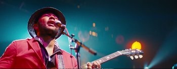 Movie still from “La La Land” (2016), directed by Damien Chazelle – A man with a hat on playing a guitar; Close Up shot, Low angle