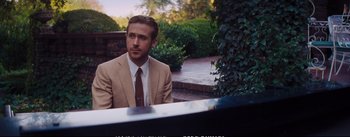 Movie still from “La La Land” (2016), directed by Damien Chazelle – A man in a suit sitting at a table outside; Medium shot, Over the shoulder angle