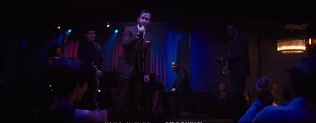 Movie still from “La La Land” (2016), directed by Damien Chazelle – A man in a suit and tie singing into a microphone; Wide shot, Over the shoulder angle