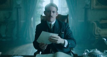 Movie still from “Lady Chatterley's Lover” (2022), directed by Laure de Clermont-Tonnerre – A man sitting in a chair holding a piece of paper; Medium shot, Low angle