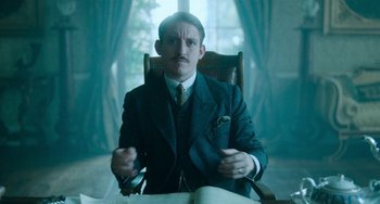 Movie still from “Lady Chatterley's Lover” (2022), directed by Laure de Clermont-Tonnerre – A man sitting in a chair holding a cell phone; Medium shot, Low angle