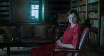 Movie still from “Lady Chatterley's Lover” (2022), directed by Laure de Clermont-Tonnerre – A woman in a red dress sitting in a chair in a living room; Medium shot, High angle