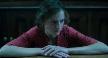 Movie still from “Lady Chatterley's Lover” (2022), directed by Laure de Clermont-Tonnerre – A woman sitting at a wooden table with her hands crossed; Close Up shot, High angle