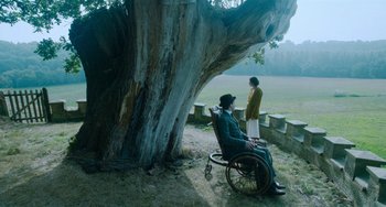 Movie still from “Lady Chatterley's Lover” (2022), directed by Laure de Clermont-Tonnerre – A man sitting in a wheelchair next to a tree; Wide shot, High angle