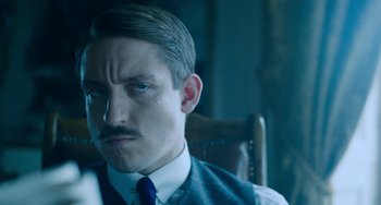 Movie still from “Lady Chatterley's Lover” (2022), directed by Laure de Clermont-Tonnerre – A person sitting in a chair wearing a tie; Close Up shot, Over the shoulder angle