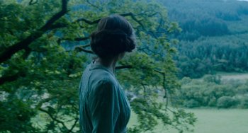 Movie still from “Lady Chatterley's Lover” (2022), directed by Laure de Clermont-Tonnerre – A woman standing in front of a tree looking out over a valley; Medium shot, Over the shoulder angle
