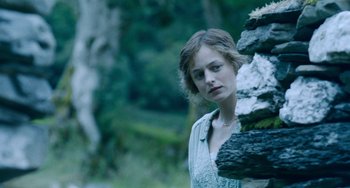 Movie still from “Lady Chatterley's Lover” (2022), directed by Laure de Clermont-Tonnerre – A woman standing next to a pile of rocks in the woods; Close Up shot, Over the shoulder angle