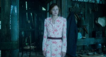 Movie still from “Lady Chatterley's Lover” (2022), directed by Laure de Clermont-Tonnerre – A woman in a floral dress standing in front of a building; Medium shot, Low angle