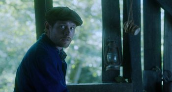 Movie still from “Lady Chatterley's Lover” (2022), directed by Laure de Clermont-Tonnerre – A man wearing a green hat and a blue shirt; Medium shot, Low angle