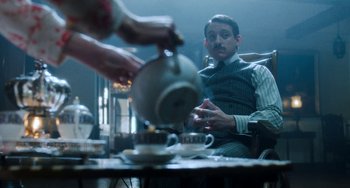 Movie still from “Lady Chatterley's Lover” (2022), directed by Laure de Clermont-Tonnerre – A man sitting at a table pouring tea into a tea pot; Medium shot, Over the shoulder angle