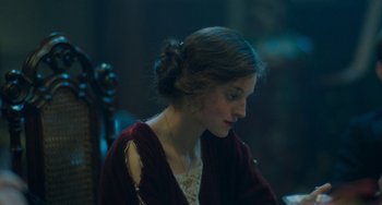 Movie still from “Lady Chatterley's Lover” (2022), directed by Laure de Clermont-Tonnerre – A woman sitting in front of a wooden table; Close Up shot, Over the shoulder angle