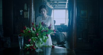 Movie still from “Lady Chatterley's Lover” (2022), directed by Laure de Clermont-Tonnerre – A woman standing in front of a table with a vase of flowers; Medium shot, Over the shoulder angle