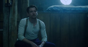 Movie still from “Lady Chatterley's Lover” (2022), directed by Laure de Clermont-Tonnerre – A man sitting on the ground wearing suspenders; Medium shot, Low angle