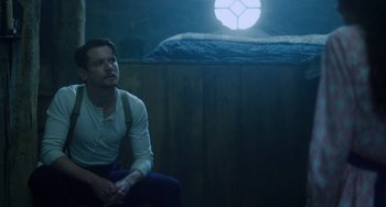 Movie still from “Lady Chatterley's Lover” (2022), directed by Laure de Clermont-Tonnerre – A man sitting on a chair in front of a bed in a dark room; Medium shot, Low angle