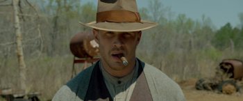 Movie still from “Lawless” (2012), directed by John Hillcoat – A man wearing a hat smoking a cigarette in a field; Close Up shot, Over the shoulder angle