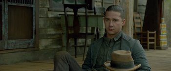 Movie still from “Lawless” (2012), directed by John Hillcoat – A man sitting on the ground with a hat on his head; Close Up shot, Over the shoulder angle