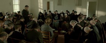 Movie still from “Lawless” (2012), directed by John Hillcoat – A group of people sitting in a room with hats on their heads; Wide shot, High angle