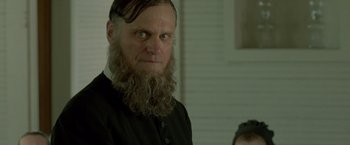 Movie still from “Lawless” (2012), directed by John Hillcoat – A man with a long beard is looking at the camera; Close Up shot, Over the shoulder angle