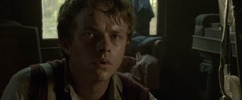 Movie still from “Lawless” (2012), directed by John Hillcoat – A young man with curly brown hair stares into the camera; Close Up shot, Over the shoulder angle