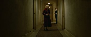 Movie still from “Lawless” (2012), directed by John Hillcoat – A woman in a red coat and a man in a black suit in a hallway; Wide shot, Low angle