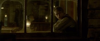 Movie still from “Lawless” (2012), directed by John Hillcoat – A young man looking out of a window at night; Medium shot, Over the shoulder angle