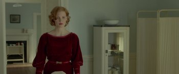 Movie still from “Lawless” (2012), directed by John Hillcoat – A woman in a red dress standing in front of a white cabinet; Medium shot, Over the shoulder angle