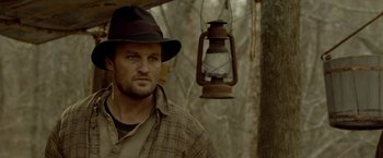 Movie still from “Lawless” (2012), directed by John Hillcoat – A man wearing a hat standing next to a lantern; Close Up shot, Over the shoulder angle