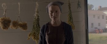 Movie still from “Lawless” (2012), directed by John Hillcoat – A woman wearing a hat standing in front of hanging plants; Medium shot, Low angle