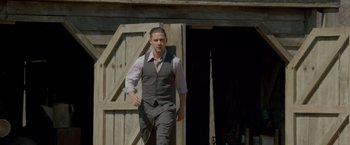 Movie still from “Lawless” (2012), directed by John Hillcoat – A man in a suit and tie standing in front of a barn door; Medium shot, Low angle