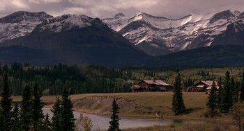 Movie still from “Legends of the Fall” (1994), directed by Edward Zwick – A house in the middle of a field with mountains in the background; Extreme Wide shot, High angle