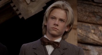 Movie still from “Legends of the Fall” (1994), directed by Edward Zwick – A young man with long blonde hair wearing a suit and bow tie; Close Up shot, Over the shoulder angle