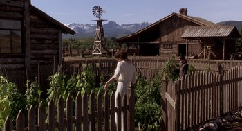 Movie still from “Legends of the Fall” (1994), directed by Edward Zwick – A woman standing in front of a wooden fence near a windmill; Wide shot, Low angle