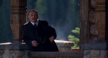 Movie still from “Legends of the Fall” (1994), directed by Edward Zwick – A man in a suit and tie standing next to a wooden post; Medium shot, Low angle