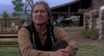 Movie still from “Legends of the Fall” (1994), directed by Edward Zwick – An older man sitting on the ground with his hands crossed; Close Up shot, Low angle
