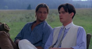 Movie still from “Legends of the Fall” (1994), directed by Edward Zwick – A couple of men sitting next to each other on a field; Medium shot, Over the shoulder angle