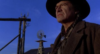 Movie still from “Legends of the Fall” (1994), directed by Edward Zwick – A man in a hat and a jacket standing in front of a windmill; Close Up shot, Low angle